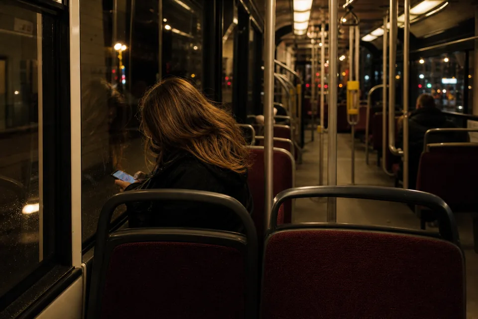 Dorosła kobieta czyta na telefonie w nocnym tramwaju, twarz odwrócona od obiektywu