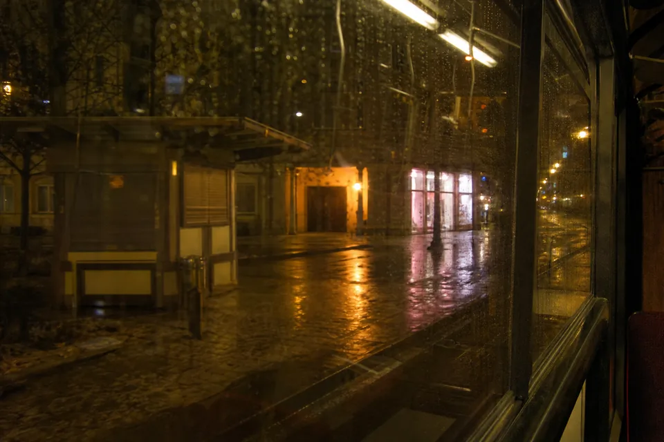 Ulica dużego miasta nocą widziana z okna tramwaju, mokry chodnik odbija światła witryn