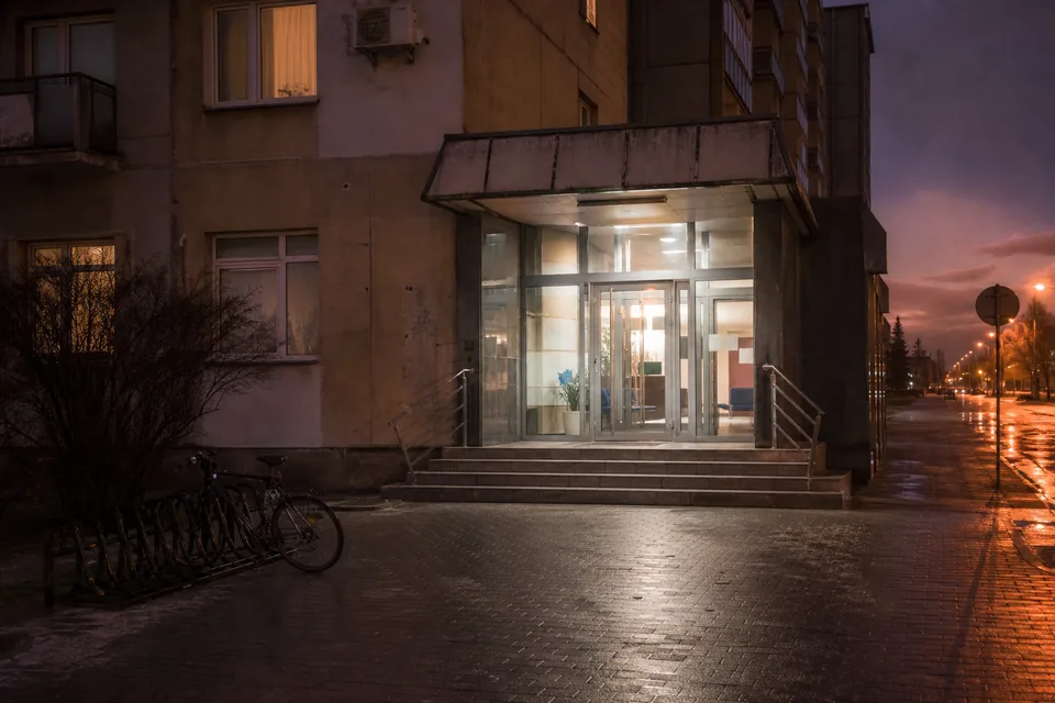 Wejście do miejskiej przychodni wieczorem, oświetlone drzwi i mokry chodnik